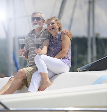 An elderly couple sitting together in a personal yacht, each holding a glass of red wine